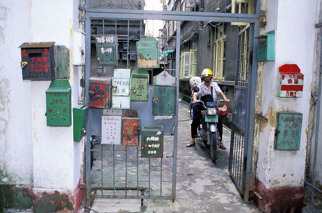 Biker on mop and mailboxes at popular housing area entrance. Guangzhou. China