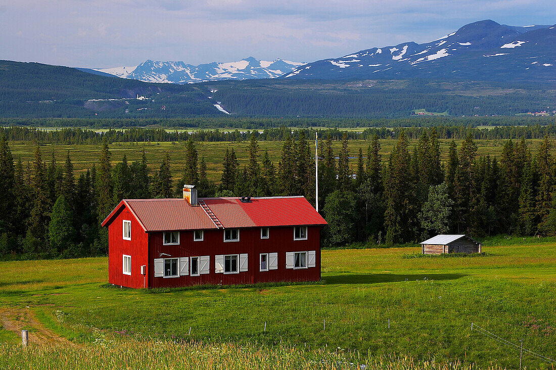 Rotes Holzhaus und Blick auf schneebedeckte Berge bei Klocka am Annsjön, Jämtland, Nordschweden