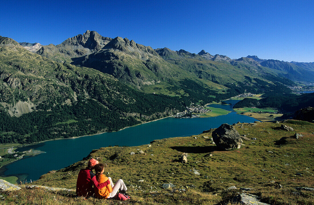 Couple sitting on alpine pasture, Lake Silvaplaner and Lake Champfer, Engadin, Grisons, Switzerland