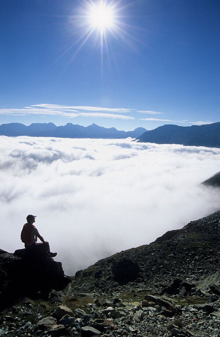 Wanderer sitzt auf einem Felse über dem Nebelmeer, Piz Julier, Oberengadin, Graubünden, Schweiz