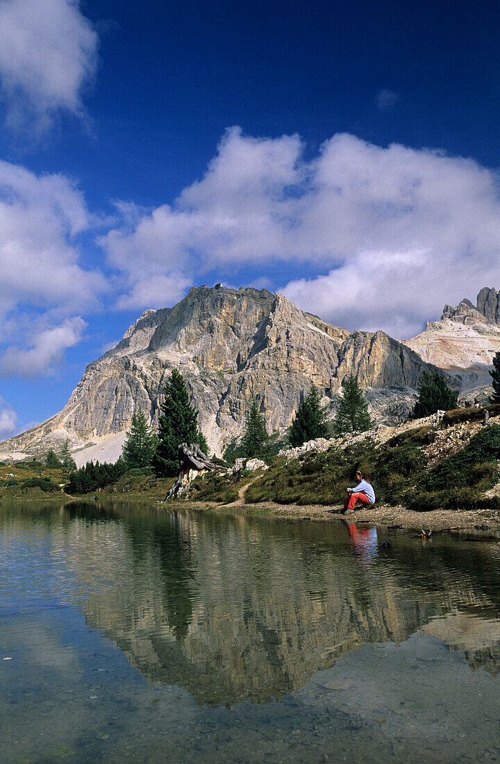 Lagazuoi above lake Lago Limedes, young woman sitting at rim, Dolomites, Italy