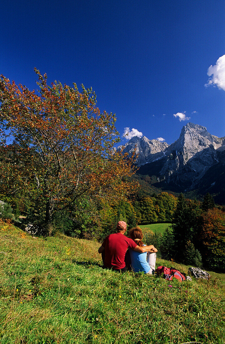 Paar sitzt auf Almwiese mit Blick Kaisergebirge, Wilder Kaiser, Tirol, Österreich