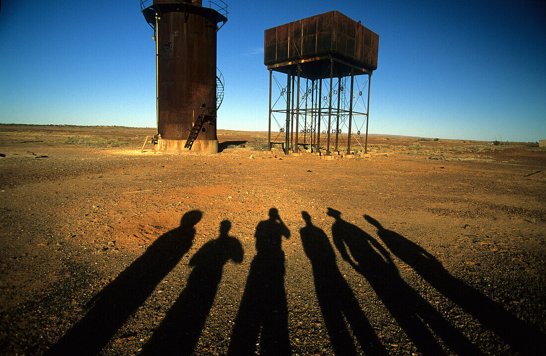 Shadows of six people standing at water tanks at the abandoned railway station of Beresford along the old Ghan railway track, Oodnadatta Track, South Australia, Australia