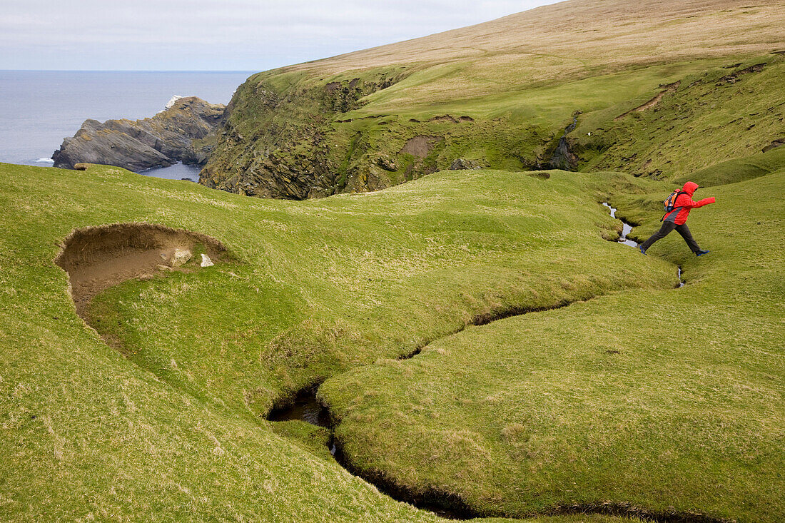 Eine Frau springt über einen Bach während einer Wanderung im Naturschutzgebiet Hermaness, Insel Unst, Shetland Islands, Schottland, Großbritannien, MR