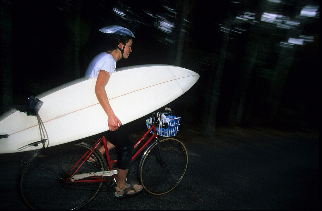 A surfer carrying his surfboard by bicycle, Lord Howe Island, Australia