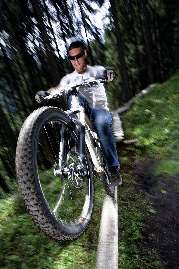 Mountainbiker fährt über eine Rampe im Wald, Oberammergau, Bayern, Deutschland