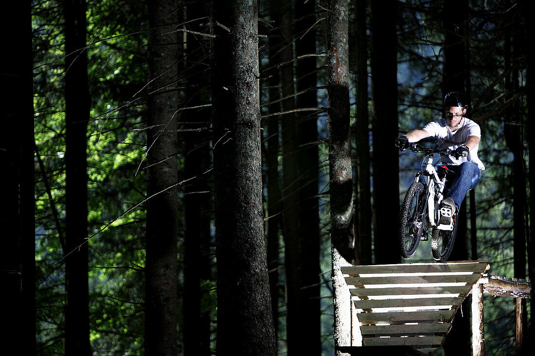Mountain biker riding over a ramp in a forest, Oberammergau, Bavaria, Germany