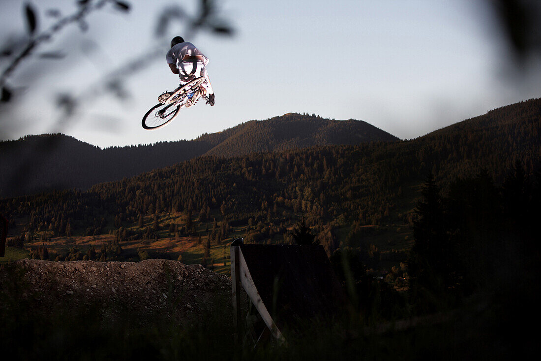 Junger Mann springt mit einem Mountainbike, Oberammergau, Bayern, Deutschland