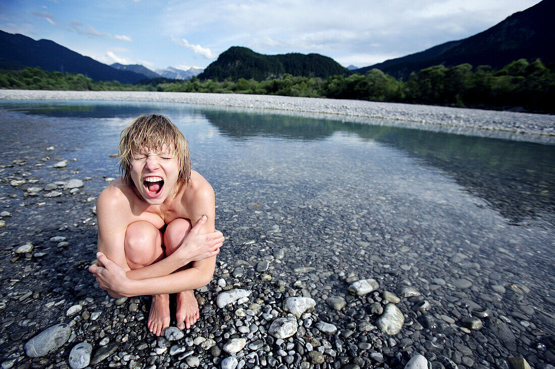 Nackte junge Frau hockt an einem Fluss und schreit, Füssen, Bayern, Deutschland