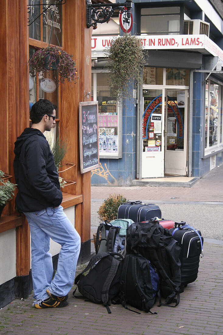 Tourist with luggage waiting near cafe in Haarlemmerdijk, Amsterdam, Holland, Netherlands