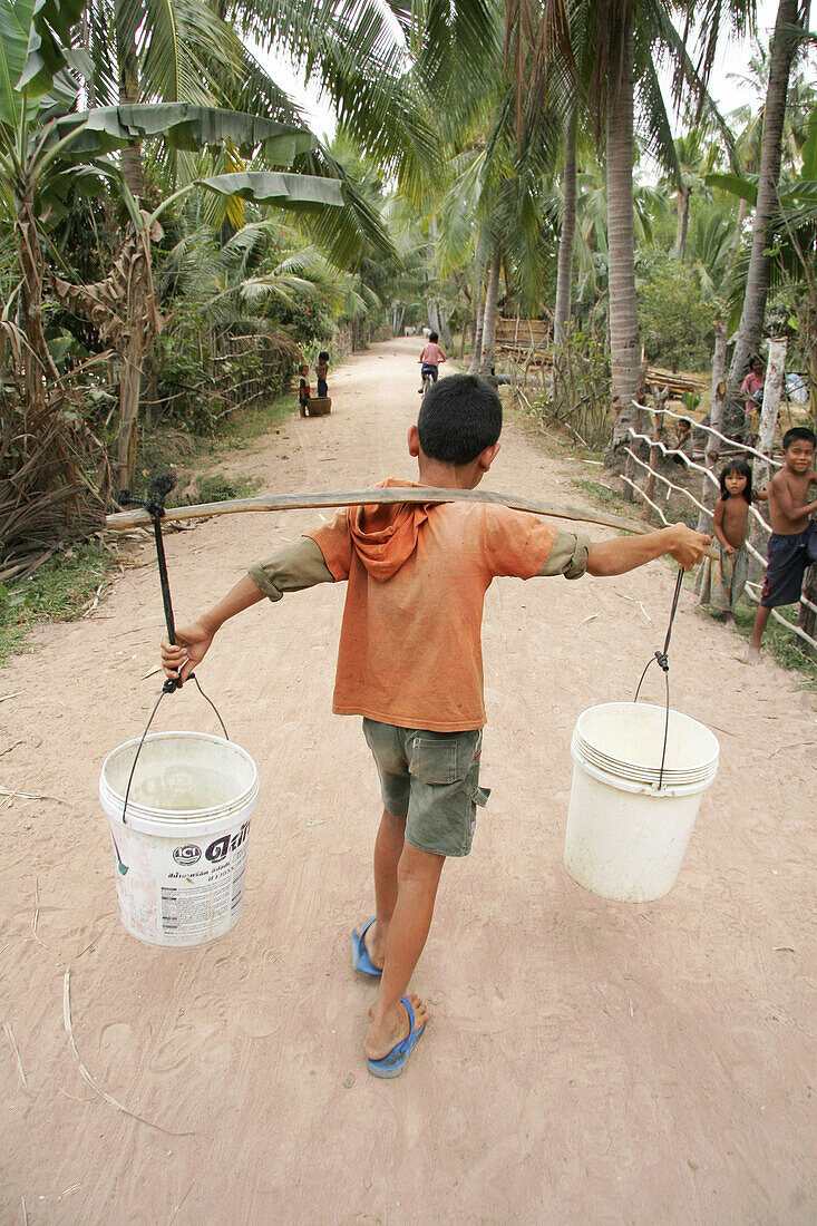 Boy carring buckets of water from a well in a village in Kampong Thom. Cambodia.