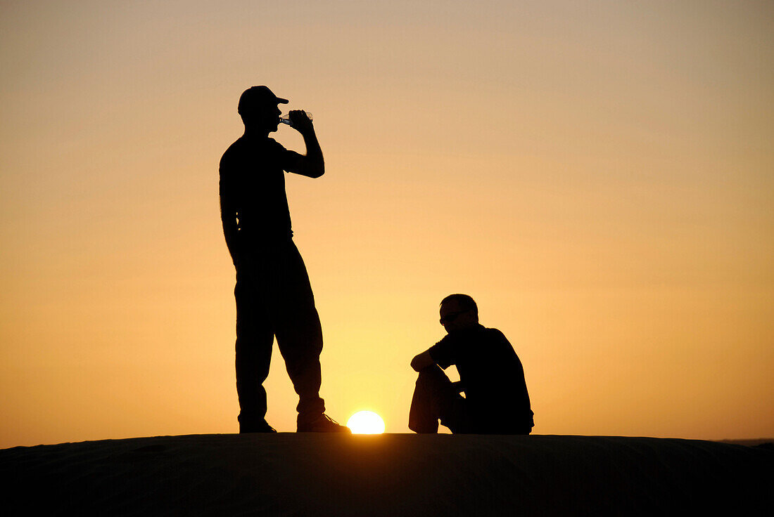 Man drinking, watching the sunset, Offroad 4x4 Sahara Desert Tour, Bebel Tembain area, Sahara, Tunisia, Africa, mr