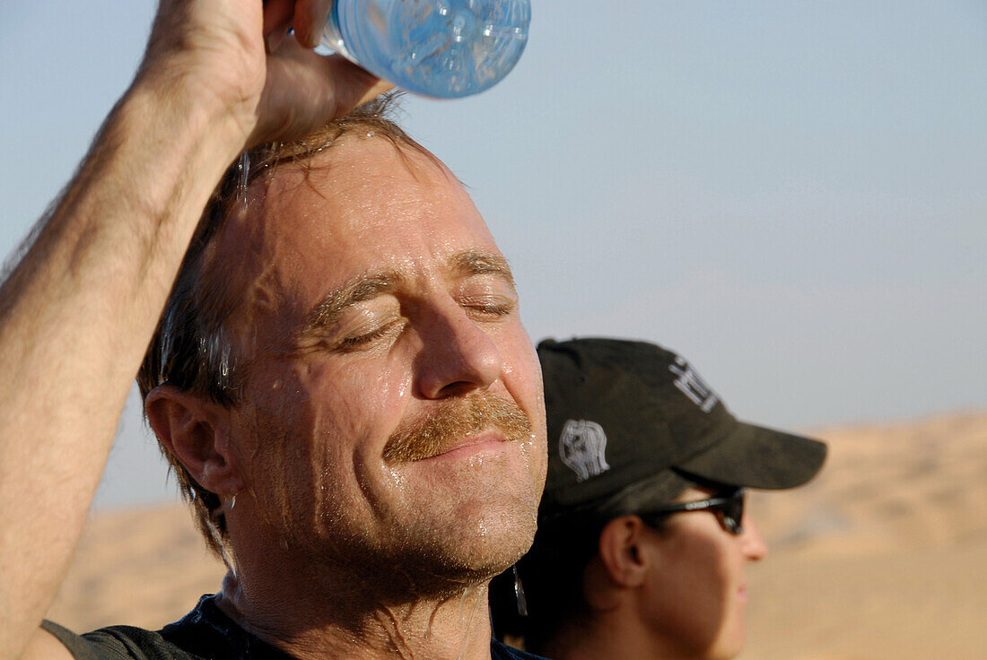 Man pouring water over his head in the hot desert sun, Cool down, Offroad Sahara Desert Tour, Bebel Tembain area, Sahara, Tunisia, Africa, mr