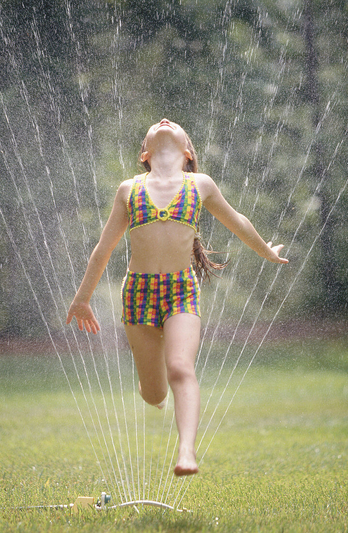 Girl running through lawn sprinkler on summer s day.