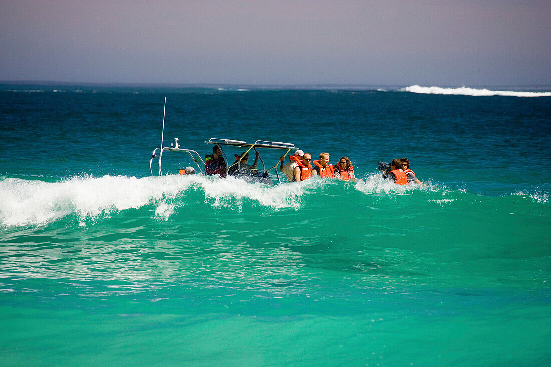 Touristen sitzen in einem Boot hinter einer Welle, Sandy Bay, Kapstadt, Südafrika