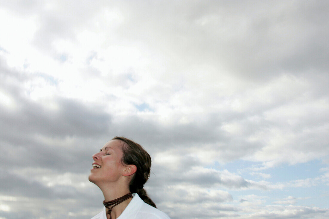Junge Frau mit geschlossen Augen steht vor Wolkenhimmel, Hessen, Deutschland