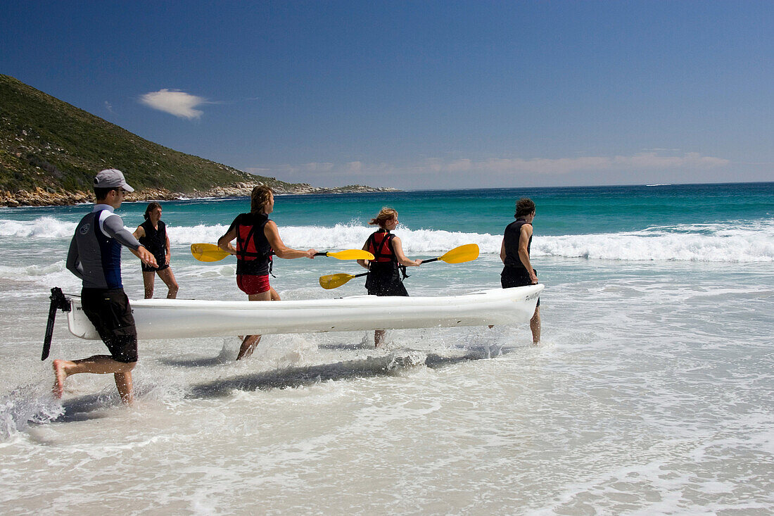 Fünf Leute tragen Boot ins Wasser, Sandy Bay Beach, Kapstadt, Südafrika, Afrika