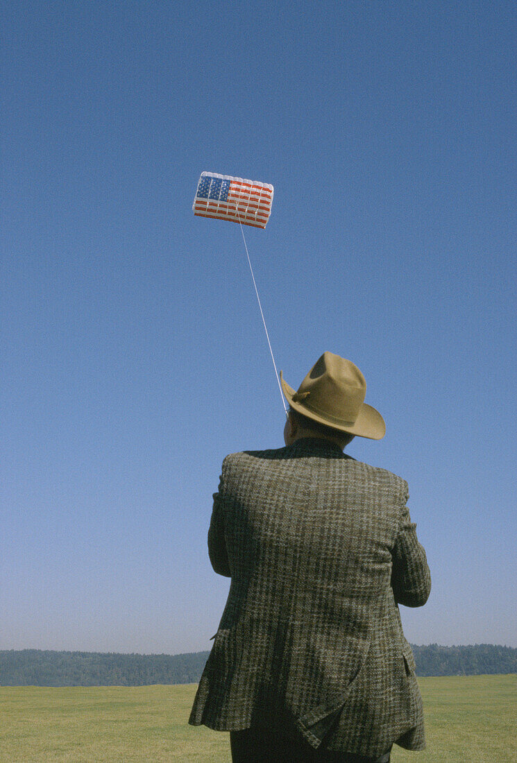  Adult, Adults, America, Amusement, Back view, Caucasian, Caucasians, Chill out, Chilling out, Color, Colour, Contemporary, Exterior, Flag, Flags, Flight, Flights, Fly, Flying, Fun, Hat, Hats, Headgear, Hobbies, Hobby, Horizon, Horizons, Human, Kite, Kite