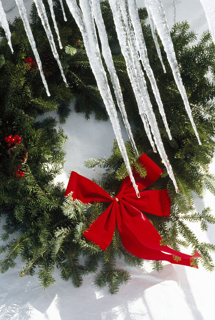 Icicles hanging in front of a Christmas wreath against a white background