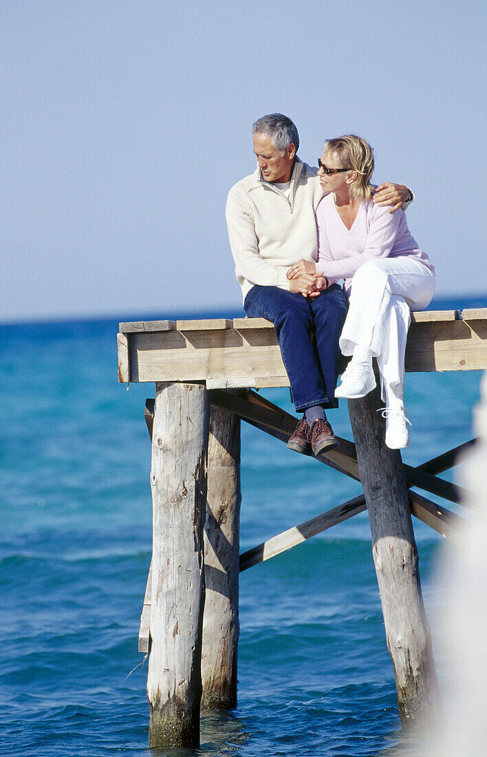 Paar, das auf einem hölzernen Steg über das Meer sitzt