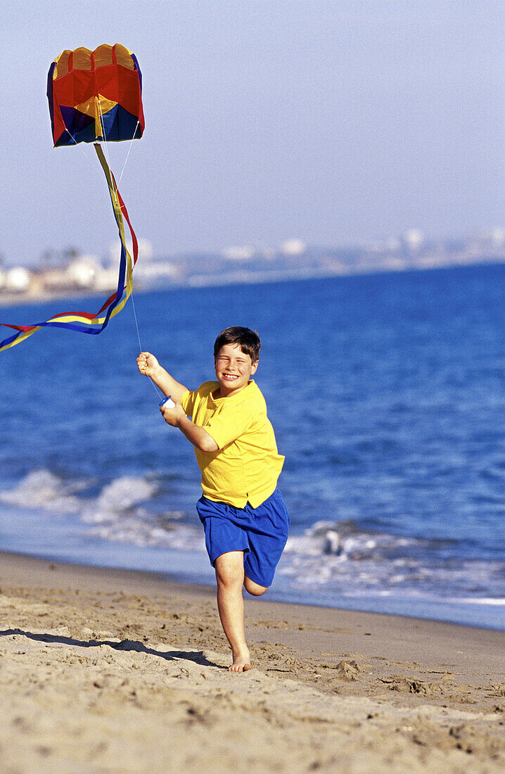 Happy boy running on beach with kite