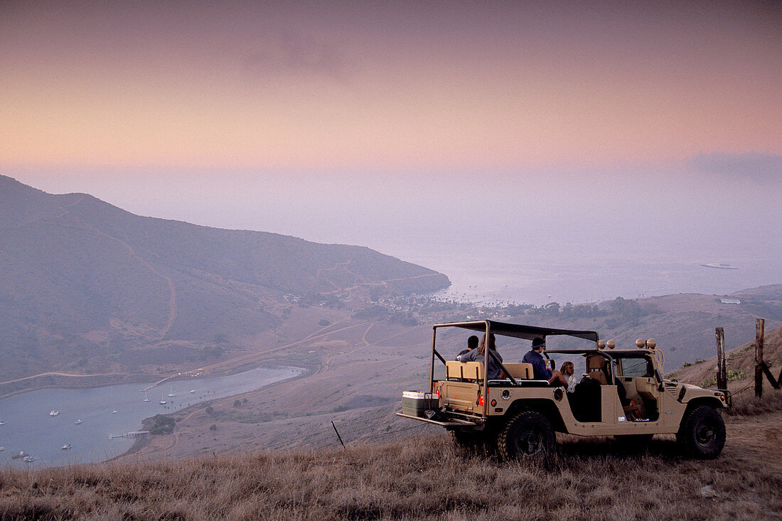 Hummer SUV driving tour in hills above Two Harbors under pink and purple evening sky, Catalina Island, California