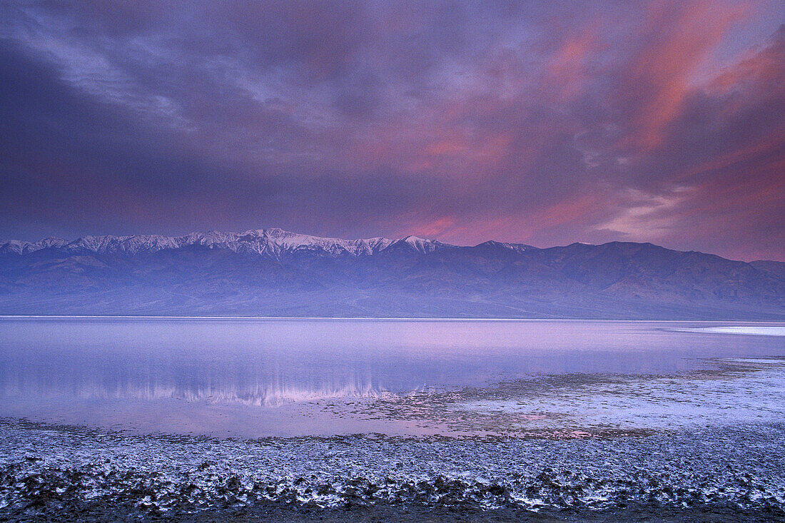 Storm clouds at sunrise over rmountains and desert flood water in salt basin near Badwater, Death Valley, California