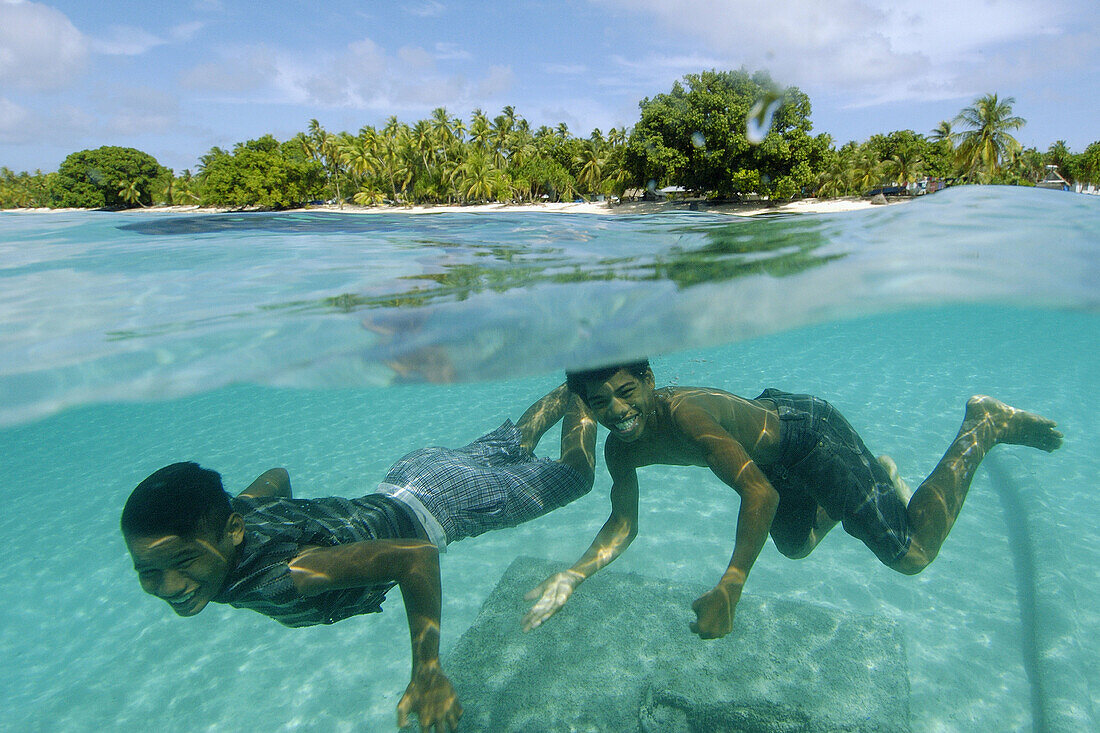 Over under image of marshallese boys smiling underwater and coconut trees lining the shore of Majikin Island, Namu atoll, Marshall Islands (N. Pacific)