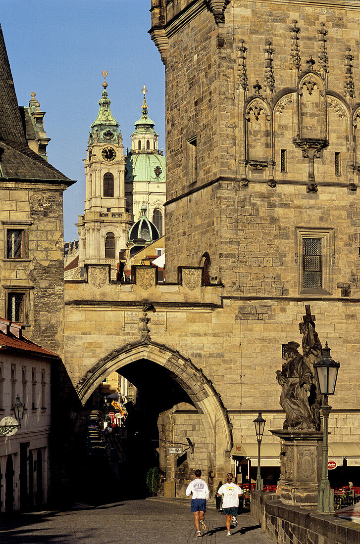Mala Strana area: Charles Bridge Tower, St. Nicholas Church, joggers. Prague. Bohemia. Czech Republic
