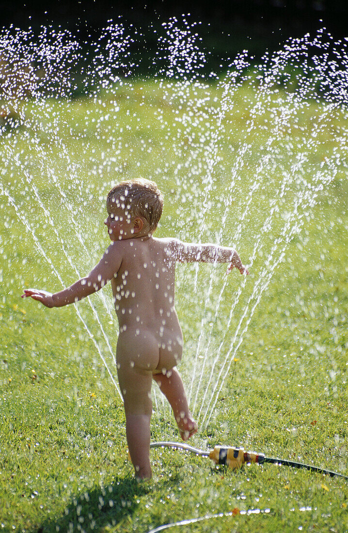 3 years old boy playing with water sprinkler