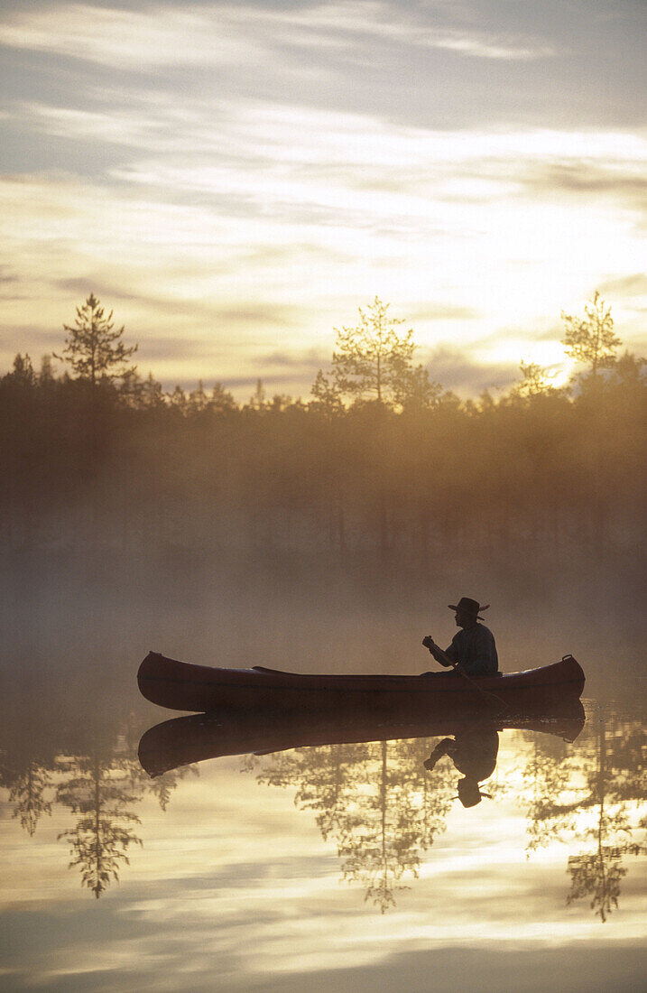A man paddle a canoe a misty summermorning at sunrise. Byske. Vasterbotten. Sweden.