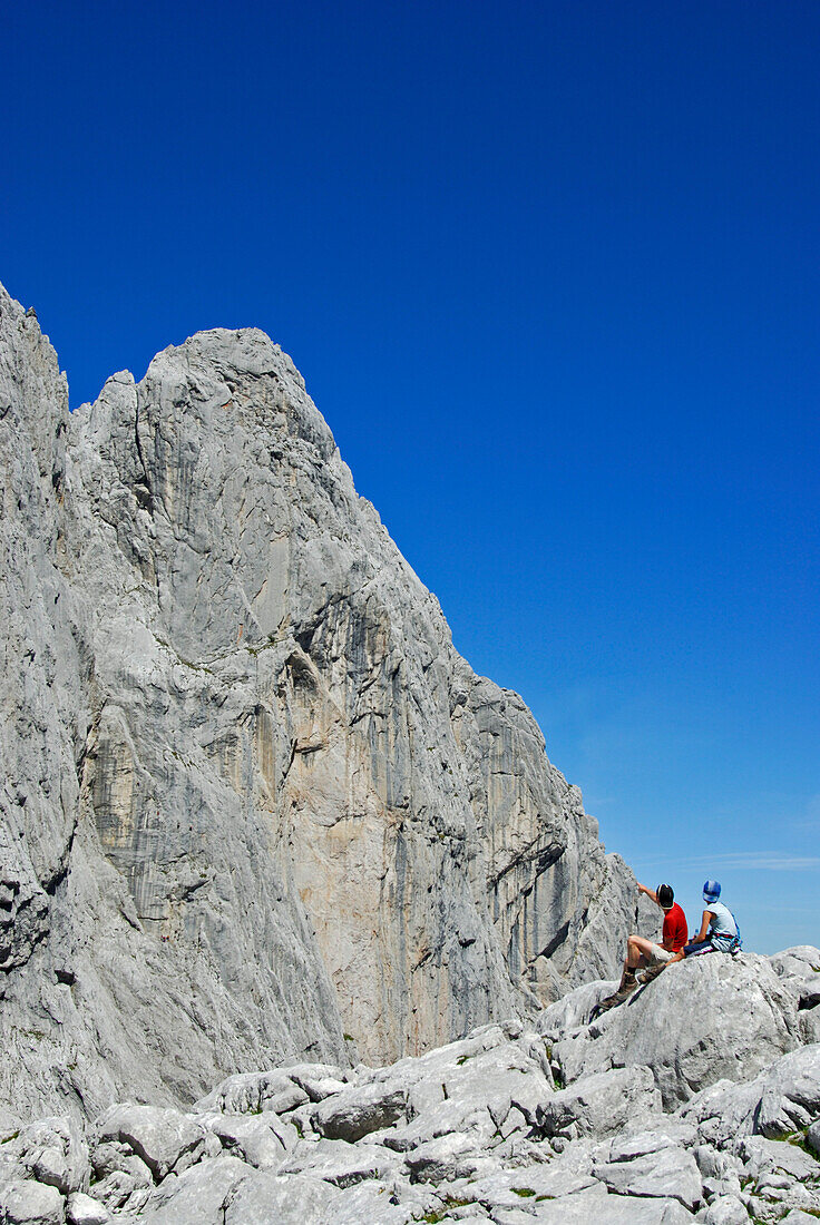 Two hikers resting at Ellmauer Tor with view to Fleischbank, Wilder Kaiser Kaiser mountain range, Tyrol, Austria