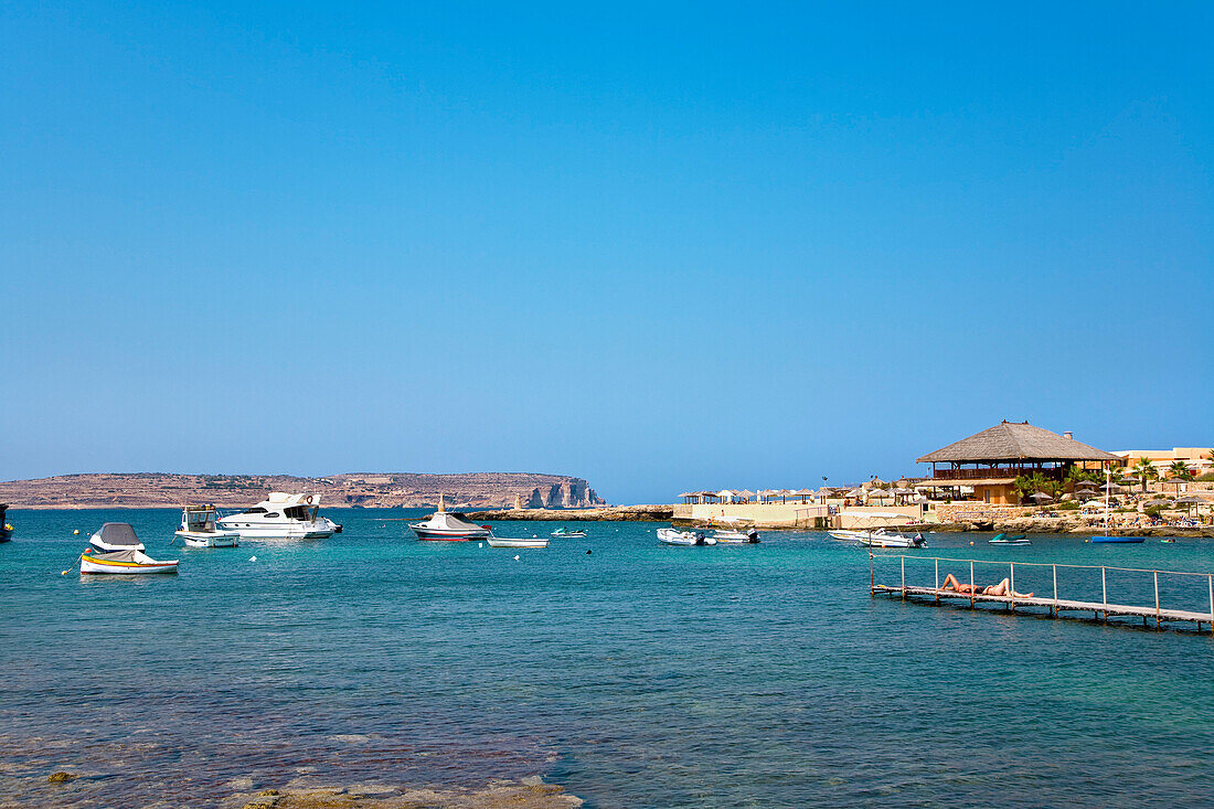 Blick auf Boote in einer Bucht und Comino unter blauem Himmel, Ramla Bay, Malta, Europa