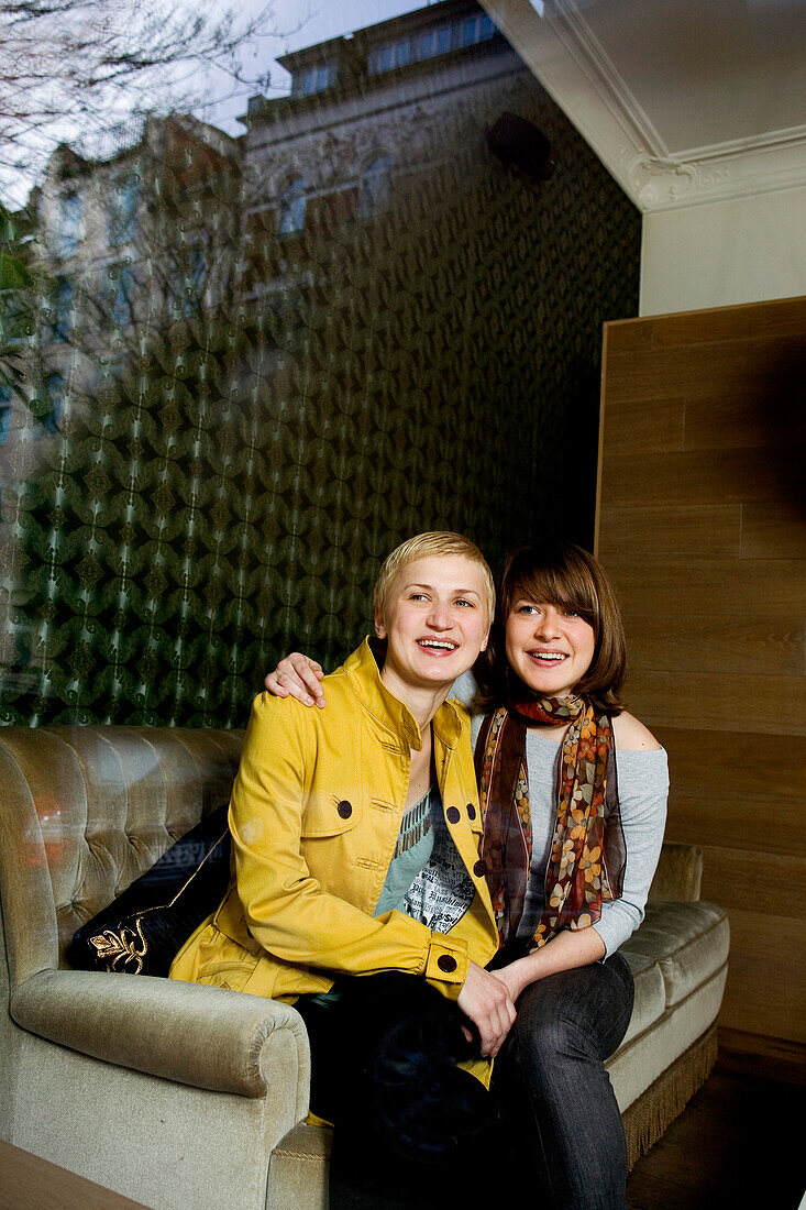 Two young woman sitting on a sofa while looking out of a window