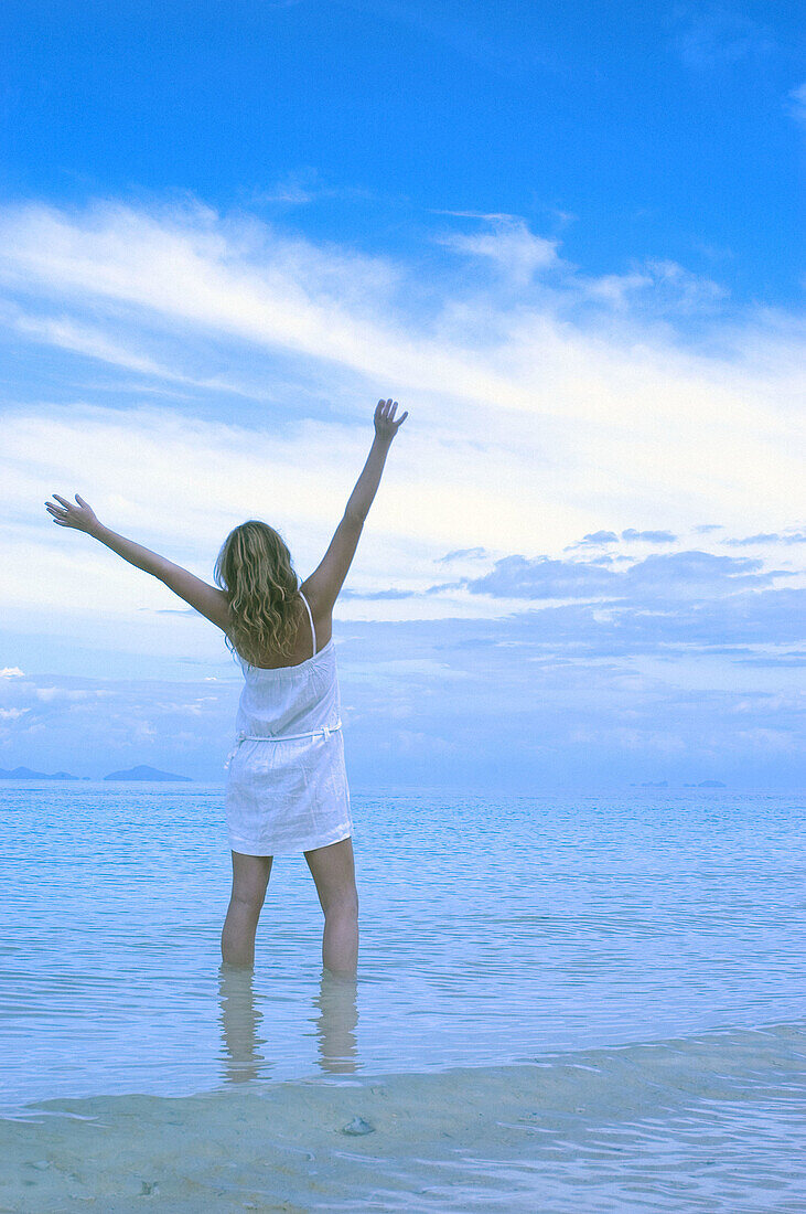  Adult, Adults, Alone, Arms raised, Back view, Beach, Beaches, Blue, Calm, Calmness, Chill out, Chilling out, Cloud, Clouds, Coast, Coastal, Color, Colour, Contemporary, Daytime, Exterior, Female, Full-body, Full-length, Gesture, Gestures, Gesturing, Happ