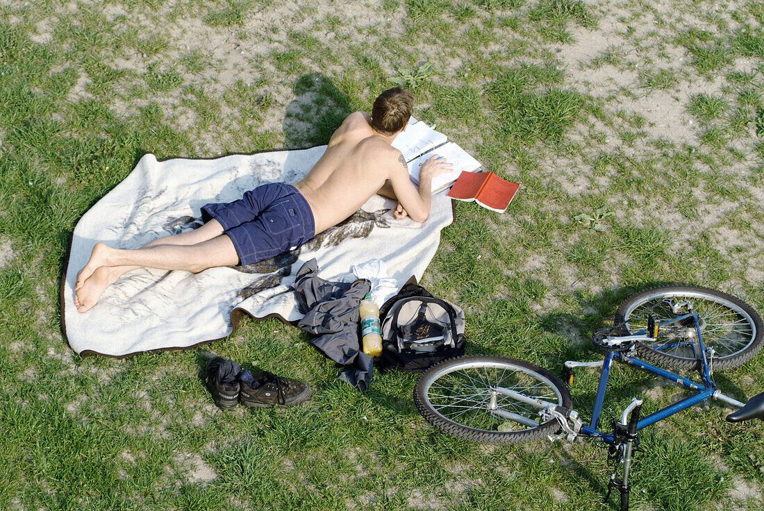 Student working while lying on am meadow. Ratisbone (Regensburg). Bavaria. Germany