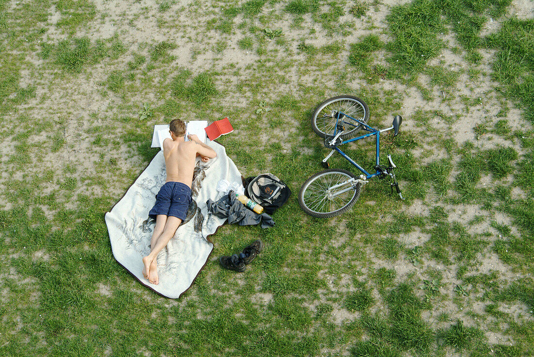 Student working while lying on am meadow. Ratisbone (Regensburg). Bavaria. Germany