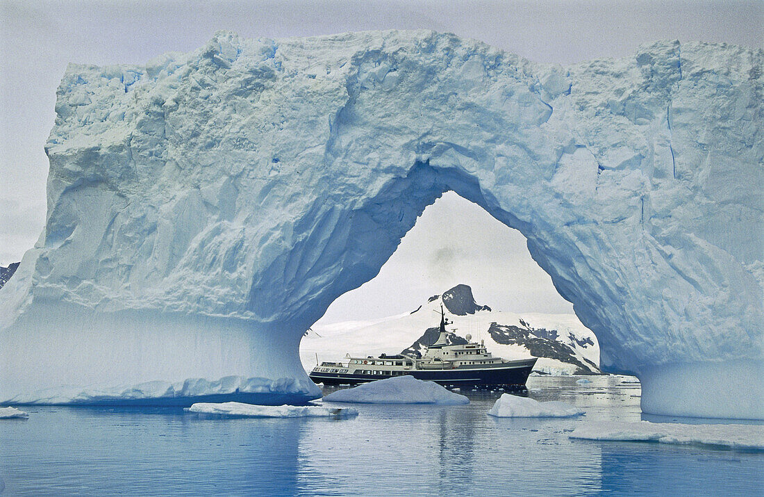Motor yatch Itasca framed in iceberg arch, Petermann Island, Antarctic peninsula