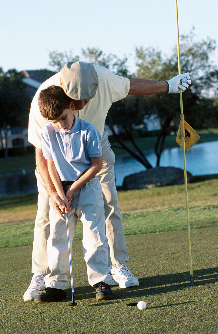 Mature man teaching boy to play golf
