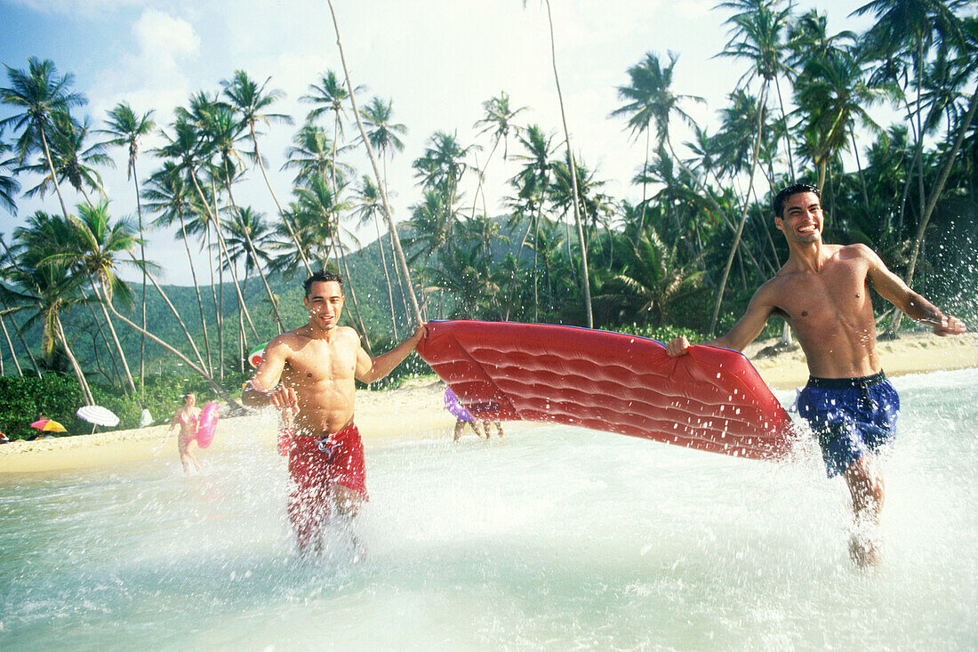 Two young men running into the water with airbed at the beach