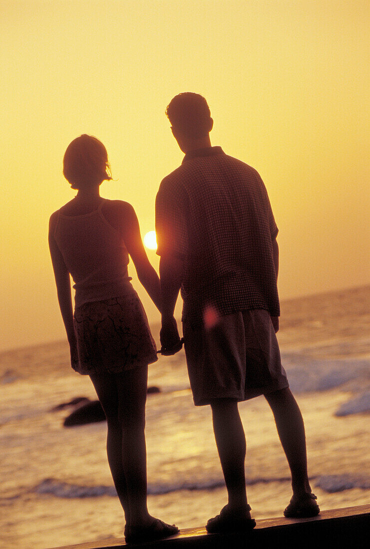 Young couple holding hands while looking the sunset at the beach, Venezuela