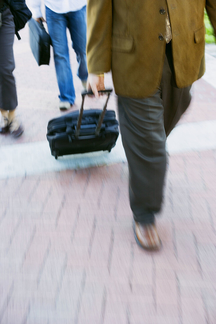 Businessman walking in the street with rolling suitcase.