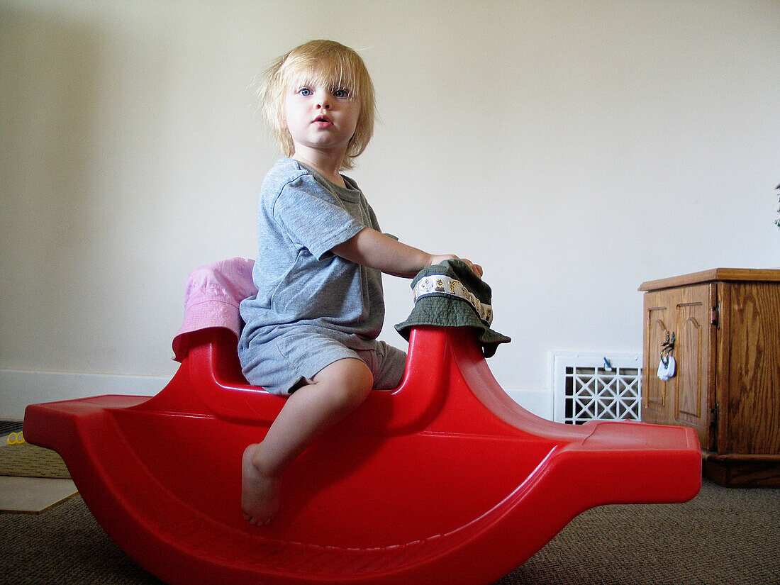 18 month old toddler playing on red rocking horse in her home