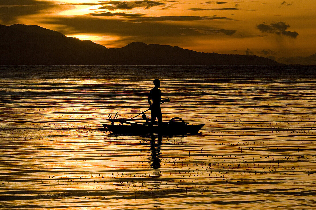 Mann paddelt stehend im Kanu bei Sonnenuntergang, Neubritannien, Papua Neuguinea, Ozeanien