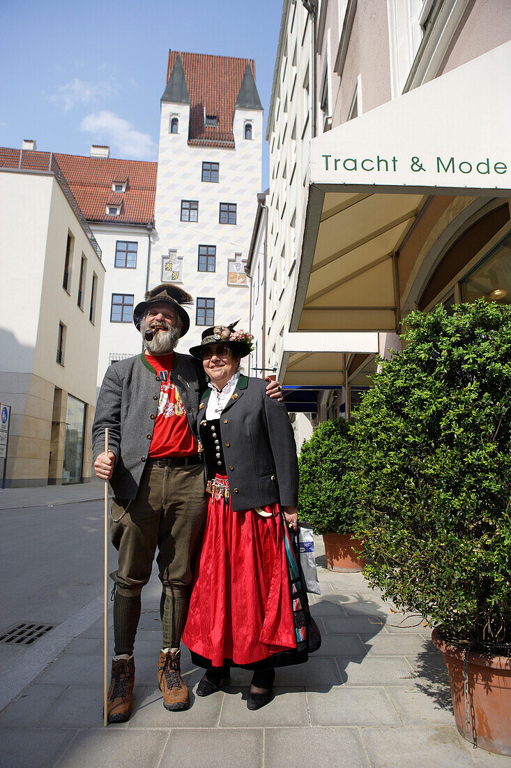 Mature couple wearing traditional costumes, tower of Alter Hof in the background, Munich, Bavaria, Germany