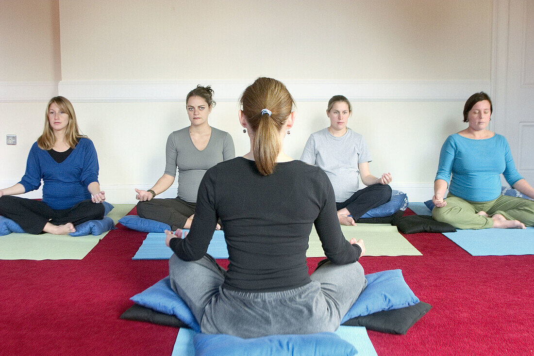 Yoga teacher sitting cross legged in front of class of four pre-natal women