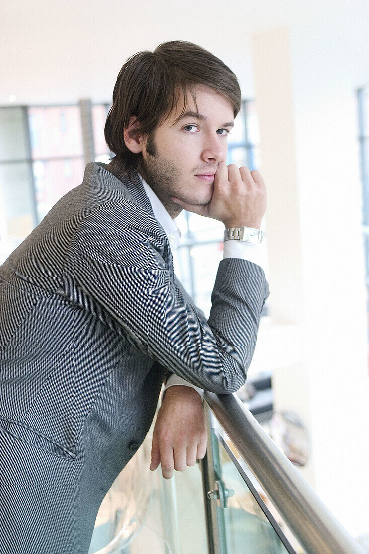 24 year old man standing against barrier serious expression, hand on chin