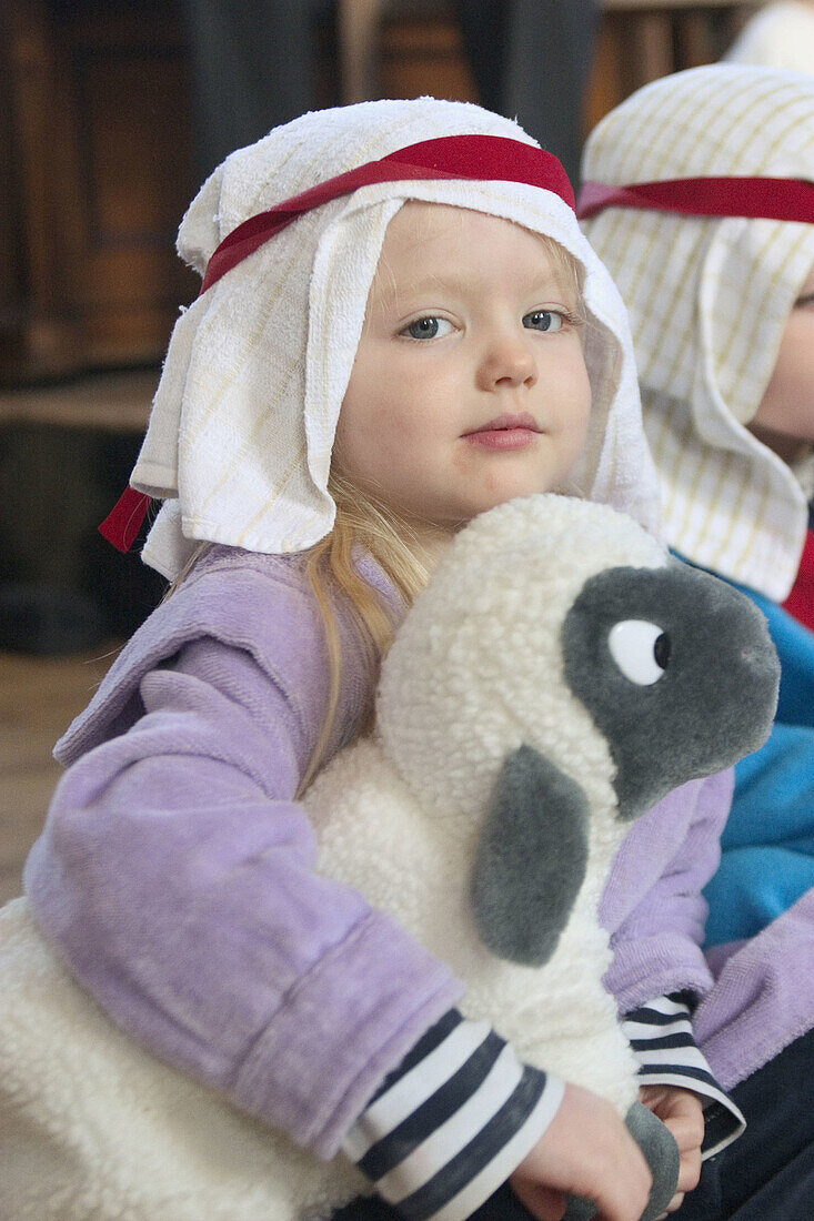 3 year old girl dressed up for a nativity play holding a toy sheep, looking into camera
