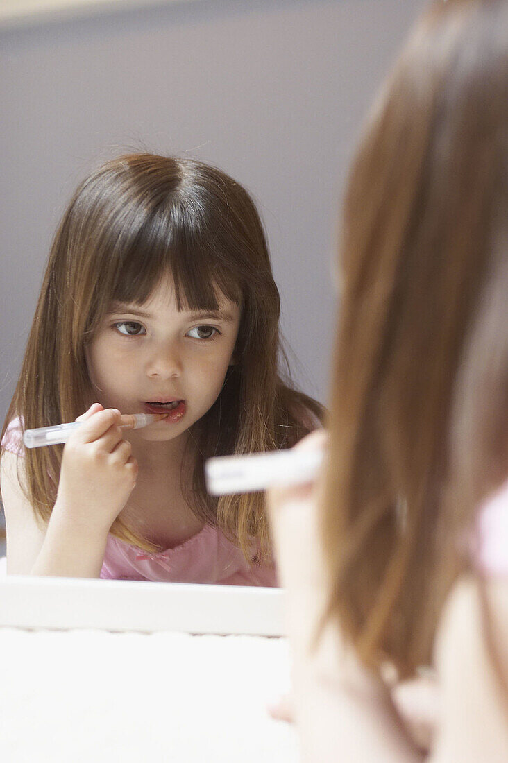 4 year old girl applying lipgloss in a mirror
