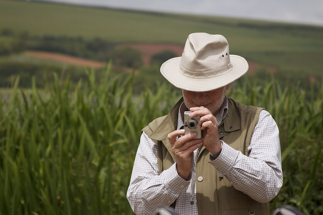 Elderly man taking a photo in some reeds by a lake, Devon, England. UK.